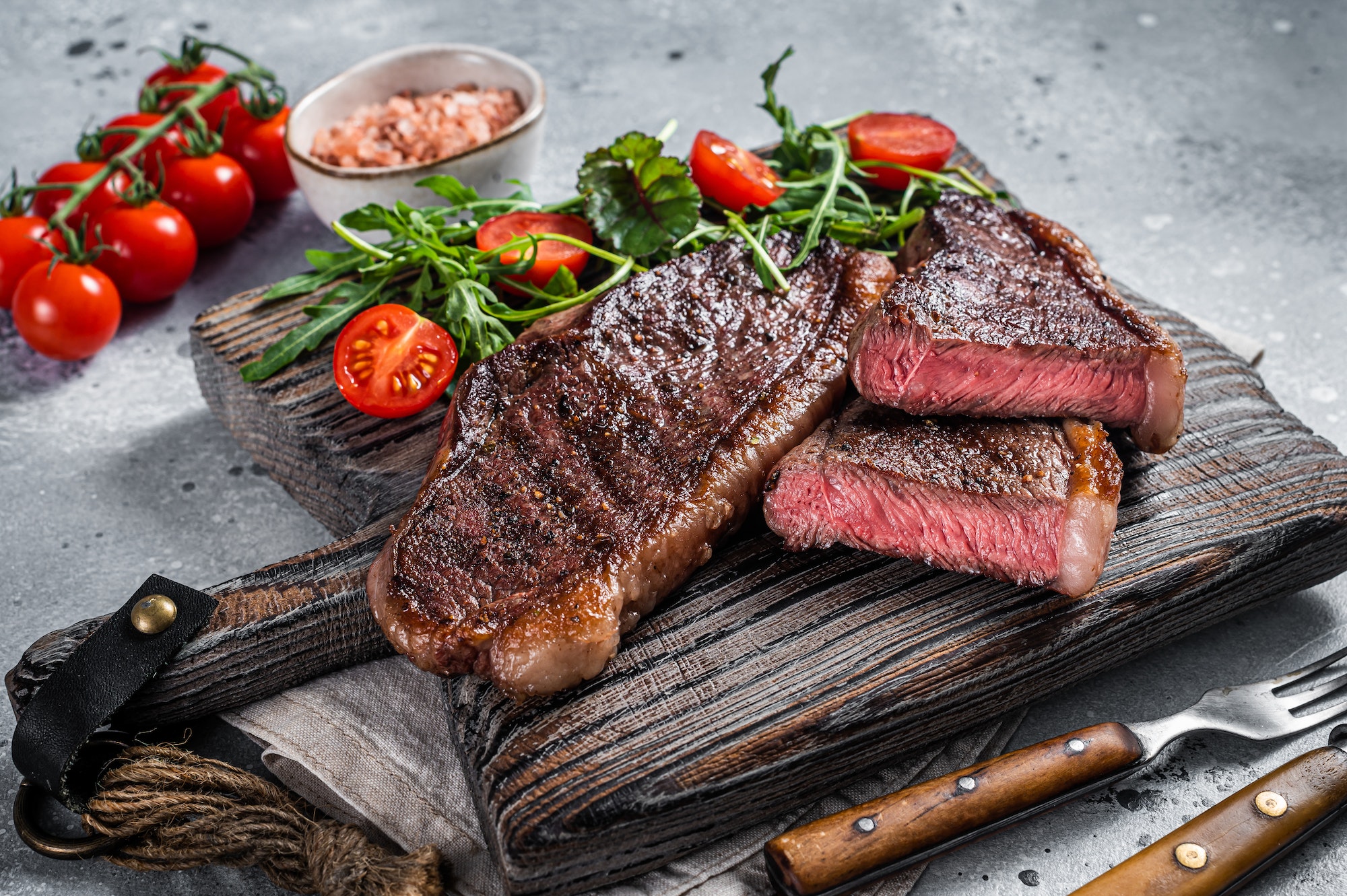 Roasted cap rump or Top sirloin beef meat steak on wooden board with salad.
